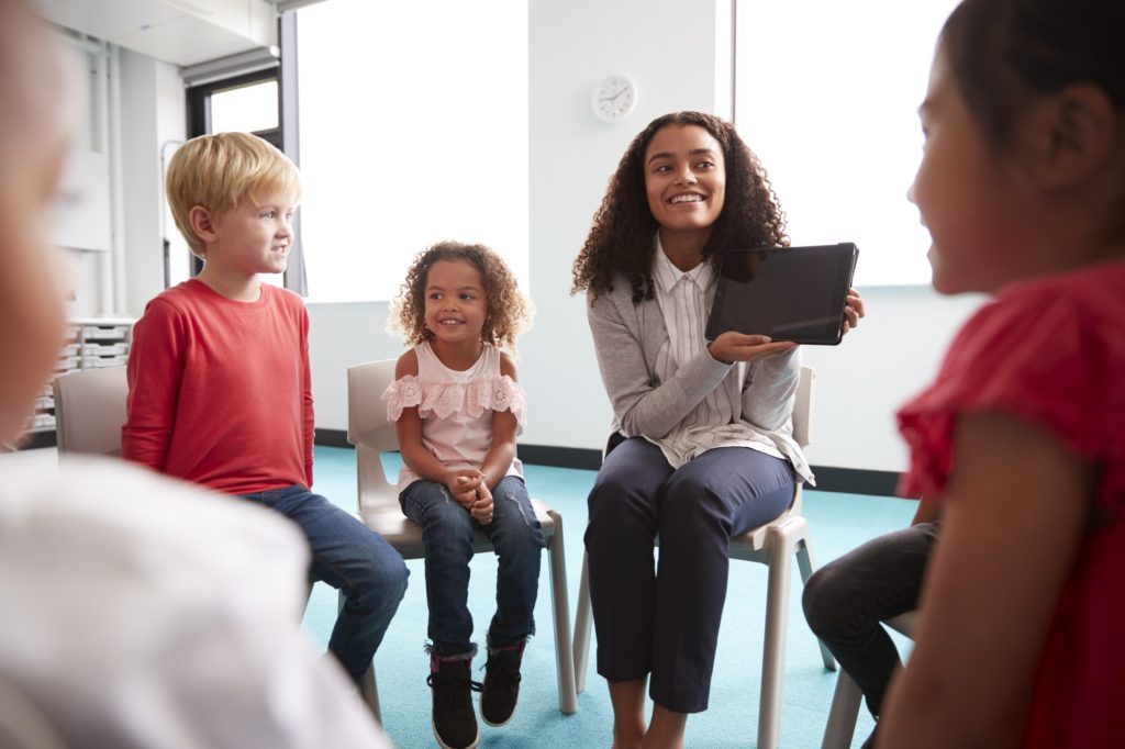 Smiling young female school teacher showing a tablet computer to infant school children